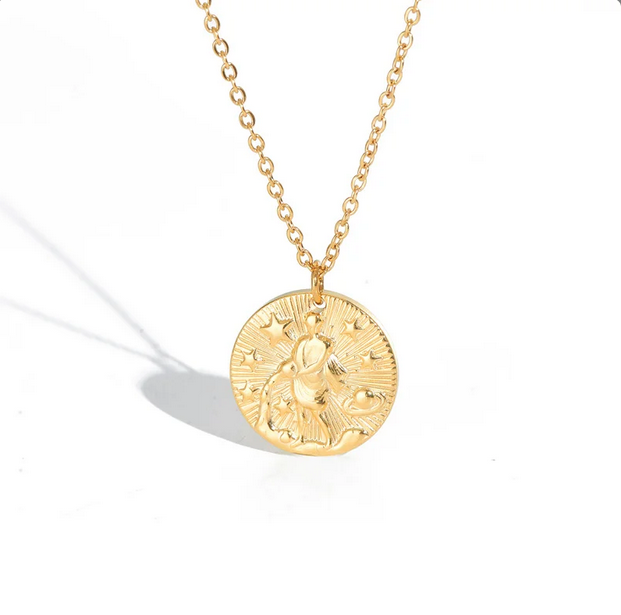 A gold necklace with a dainty chain. The necklace has a coin pendant displaying the astrological sign Aquarius of the zodiac.