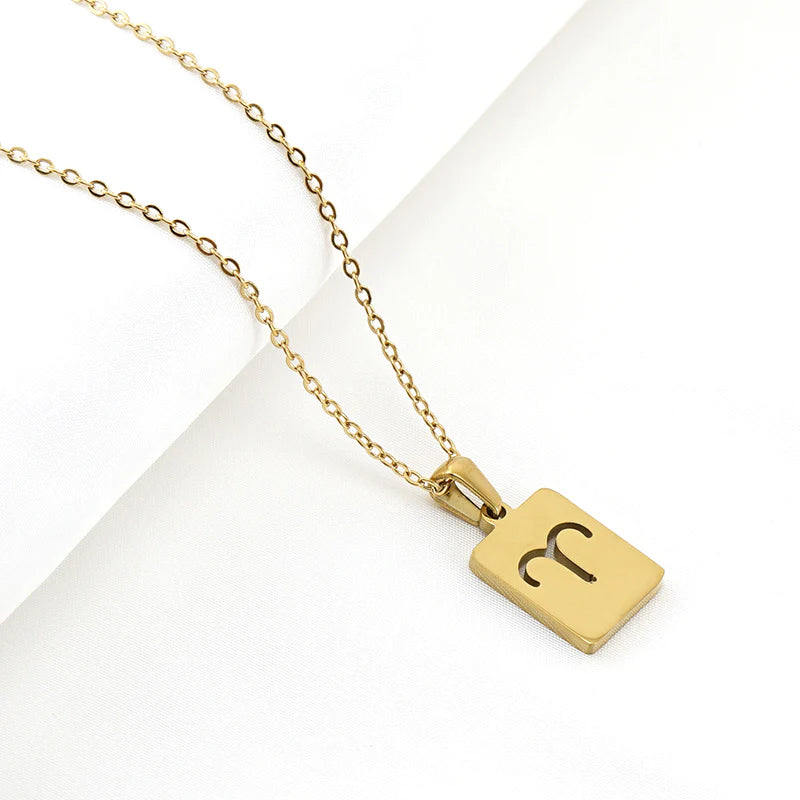 A gold necklace with a dainty chain and rectangular pendant in the Aries style. 