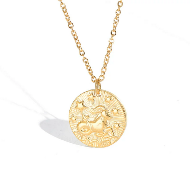 A gold necklace with a dainty chain. The necklace has a coin pendant displaying the astrological sign Capricorn of the zodiac. 