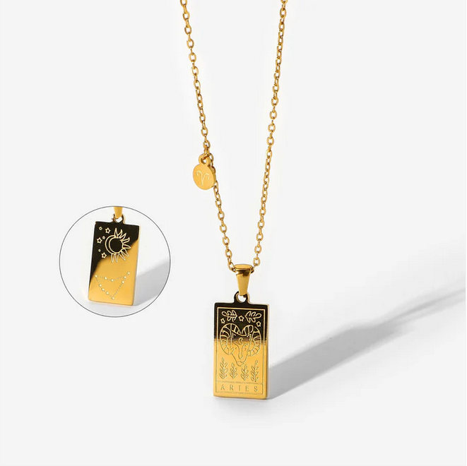 A gold necklace with a dainty chain. The necklace has a two-sided pendant in the Aries style. The front side displays the animal which represents the zodiac in laser etching with the sign spelled out in capital letters. The reverse is shown as a picture in picture image.  The reverse is in the style of the astrological constellation. There is also a small circular charm with the zodiac symbol approximately one inch above the pendant. 