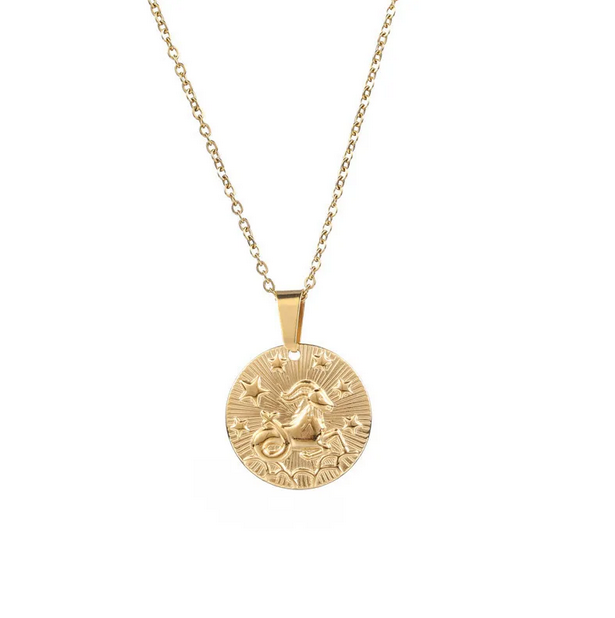 A gold necklace with a dainty chain. The necklace has a coin pendant displaying the astrological sign Capricorn of the zodiac.