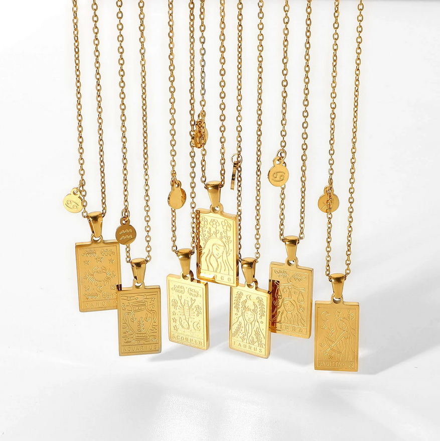 The cardinal necklances hanging with a white background, displaying seven styles of the zodiac. The necklaces are a dainty chain with a square style pendant with laser etching to create the artwork of the zodiac. 