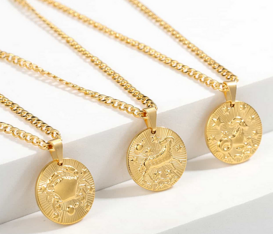 Three gold necklaces with a dainty chain. Each necklace has a coin pendant displaying one of the astrological signs of the zodiac. The first is Cancer, the second is Aries, a. Tnd the third is Capricorn. 