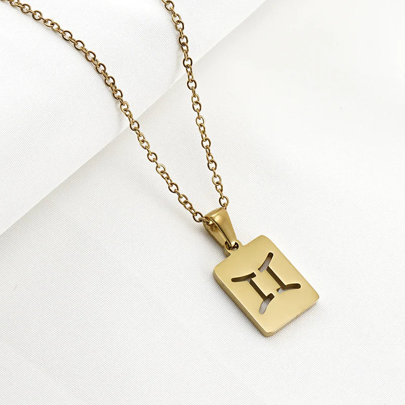 A gold necklace with a dainty chain and rectangular pendant in the Gemini style. 