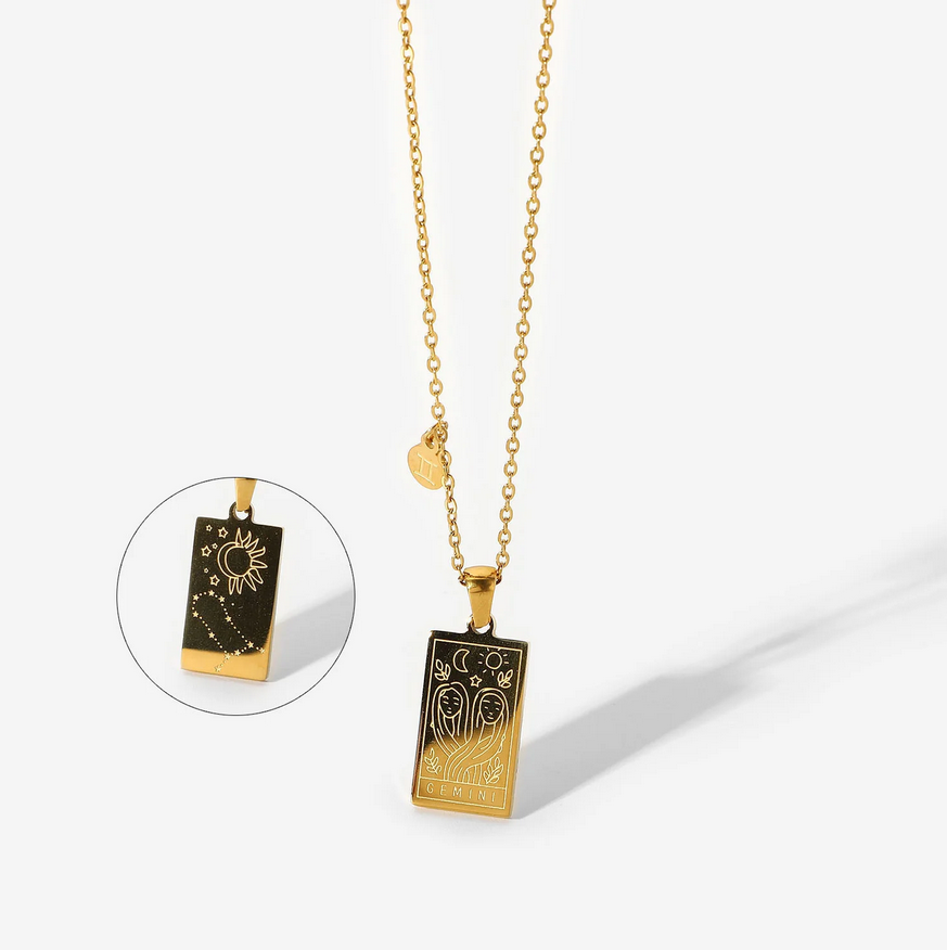 A gold necklace with a dainty chain. The necklace has a two-sided pendant in the Gemini style. The front side displays the animal which represents the zodiac in laser etching with the sign spelled out in capital letters. The reverse is shown as a picture in picture image. The reverse is in the style of the astrological constellation. There is also a small circular charm with the zodiac symbol approximately one inch above the pendant.