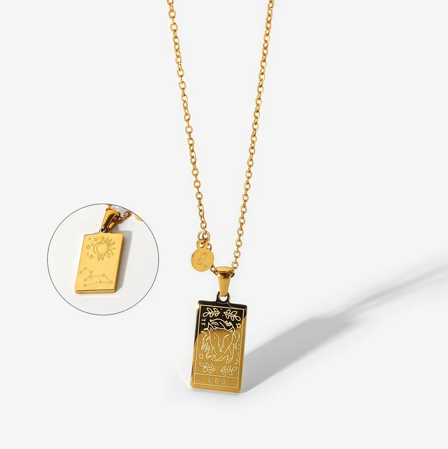 A gold necklace with a dainty chain. The necklace has a two-sided pendant in the Leo style. The front side displays the animal which represents the zodiac in laser etching with the sign spelled out in capital letters. The reverse is shown as a picture in picture image. The reverse is in the style of the astrological constellation. There is also a small circular charm with the zodiac symbol approximately one inch above the pendant.