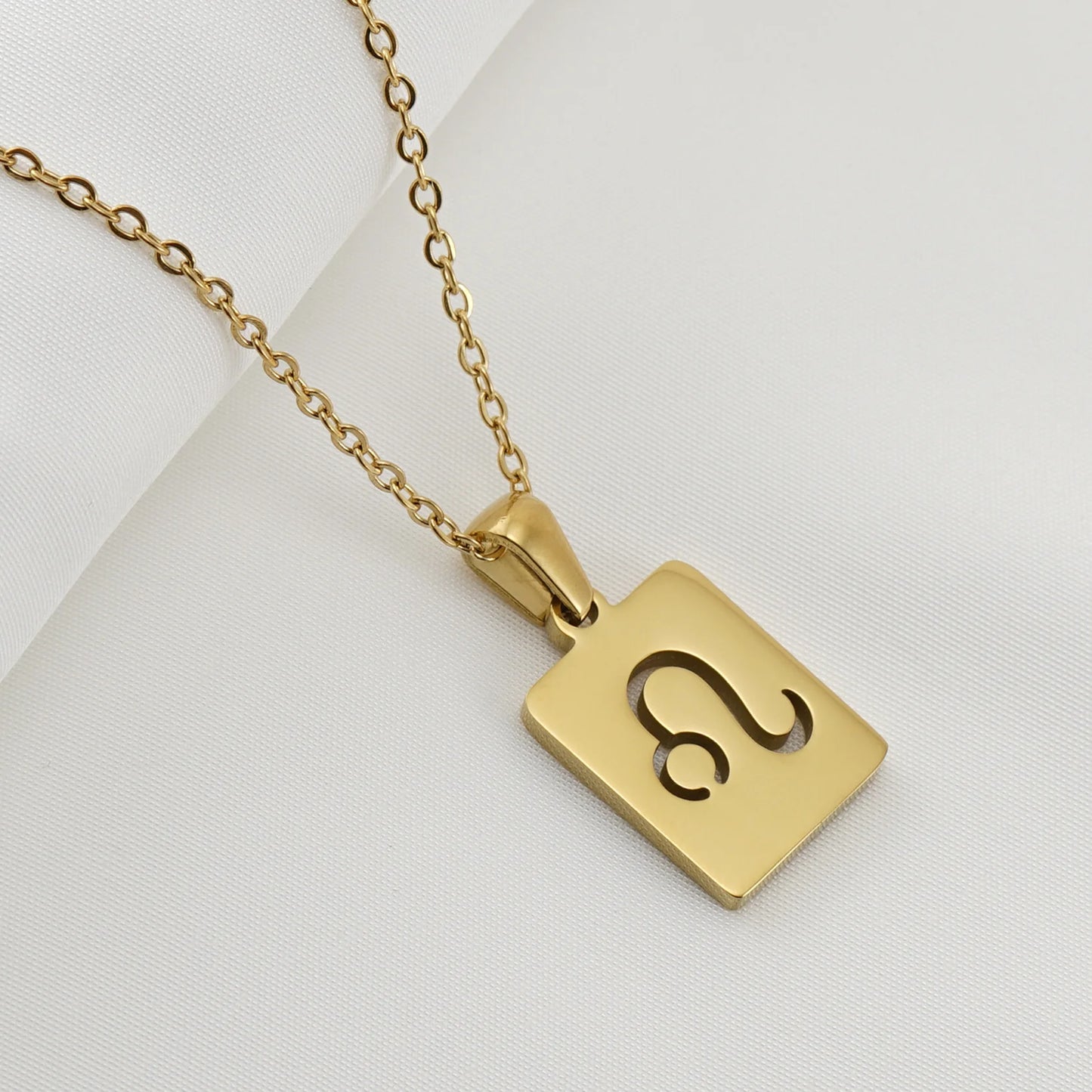 A gold necklace with a dainty chain and rectangular pendant in the Leo style. 