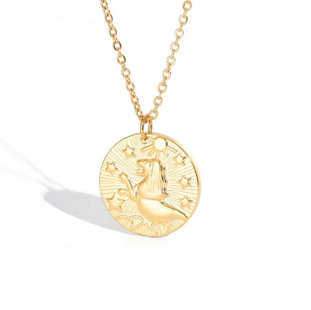 A gold necklace with a dainty chain. The necklace has a coin pendant displaying the astrological sign Leo of the zodiac.