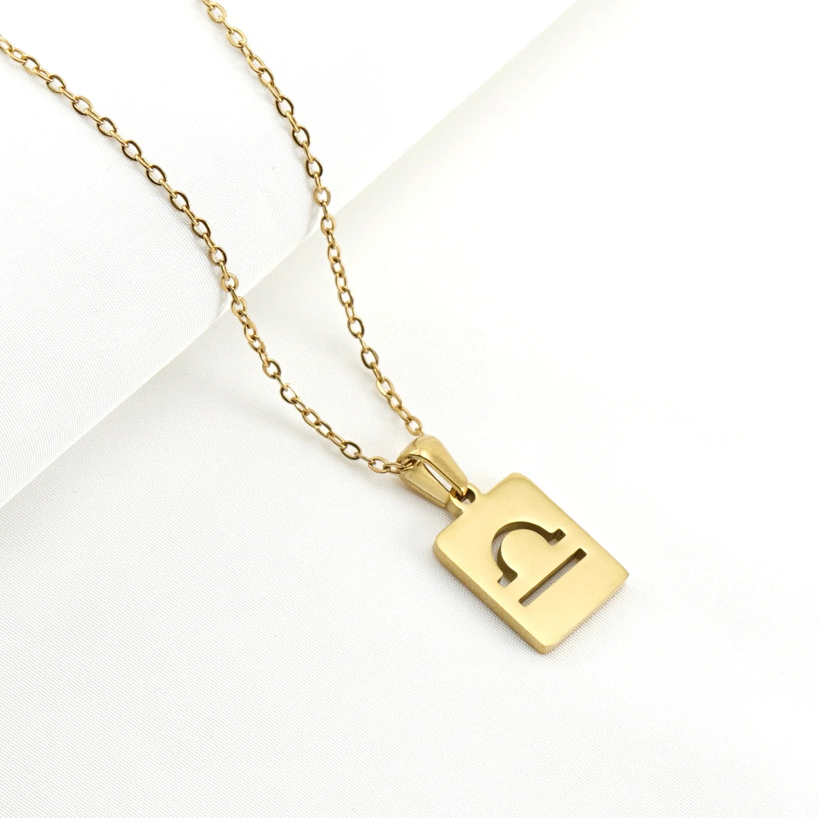 A gold necklace with a dainty chain and rectangular pendant in the Libra style. 