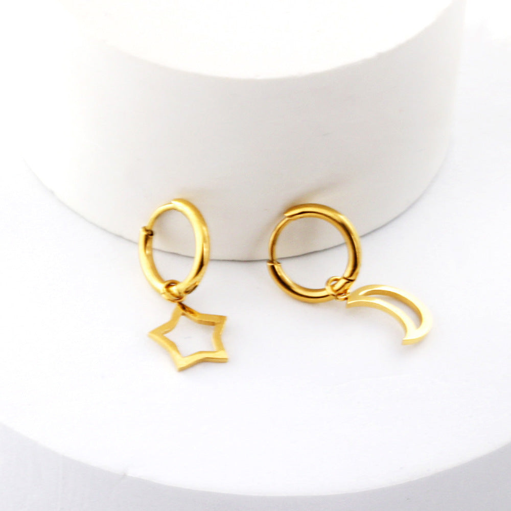 Asymmetrical gold earrings. One earring has a hollow star and the other has a hollow crescent moon. The charms are connected to a small hoop that is also gold. The earrings are prpped against a circular shape.