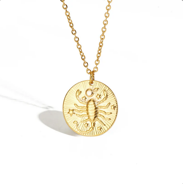 A gold necklace with a dainty chain. The necklace has a coin pendant displaying the astrological sign Cancer of the zodiac.