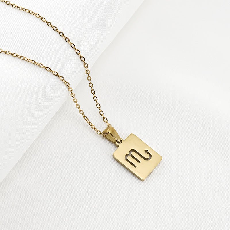 A gold necklace with a dainty chain and rectangular pendant in the Scorpio style. 