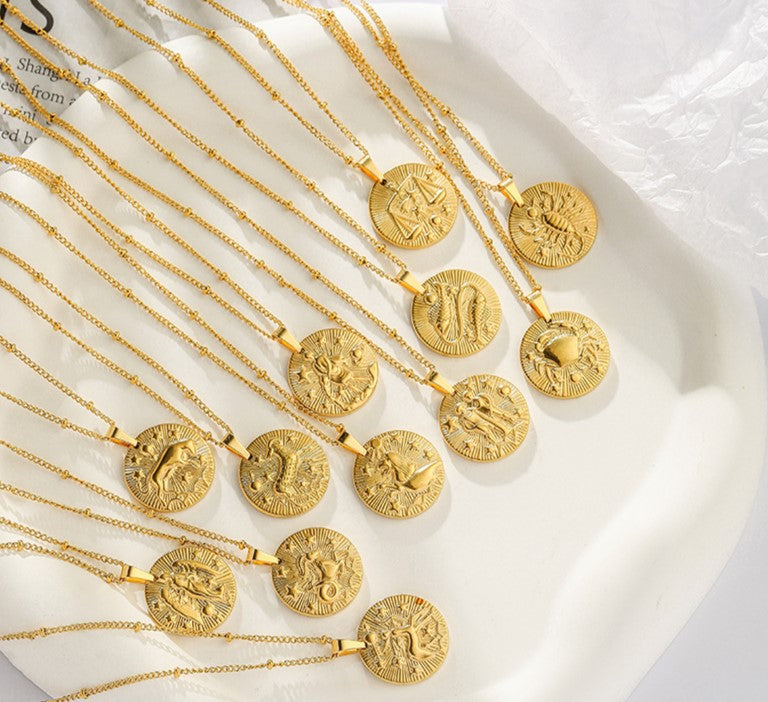 Twelve gold necklaces with a dainty chain. Each necklace has a coin pendant displaying one of the astrological signs of the zodiac. 