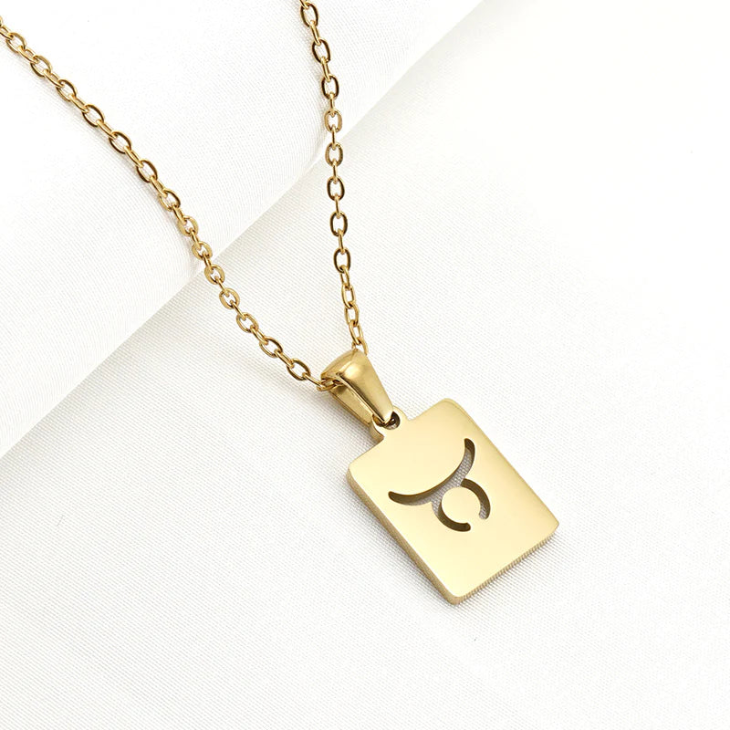 A gold necklace with a dainty chain and rectangular pendant in the Taurus style. 