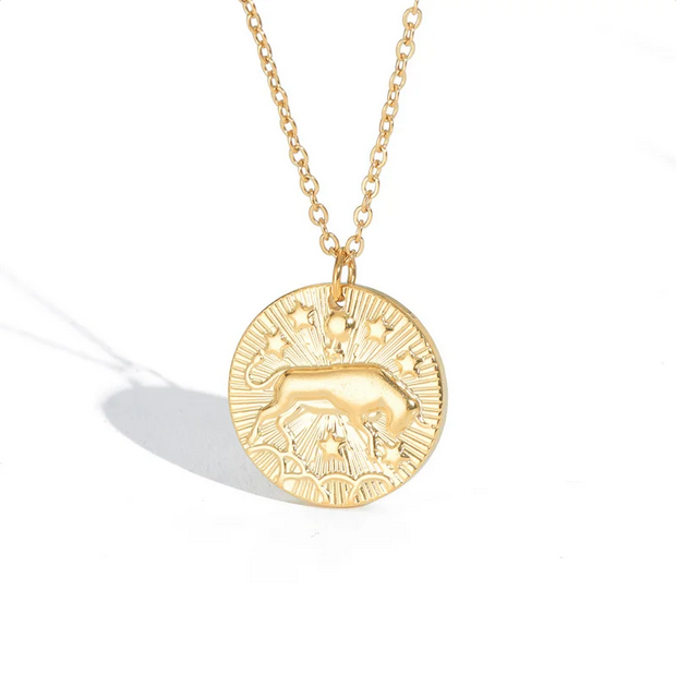 A gold necklace with a dainty chain. The necklace has a coin pendant displaying the astrological sign Taurus of the zodiac.