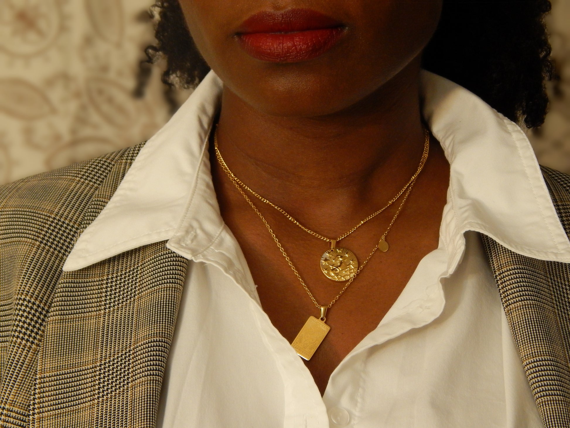 A black woman wearing the gift of two zodiac necklaces in business casual work wear. The woman is wearing both the Element necklace and Cardinal necklace. 